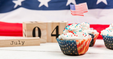 Rustic 4th of July outdoor setup with a weathered wood table, vintage lanterns, American flag accents, and cozy seating styled for a summer gathering.